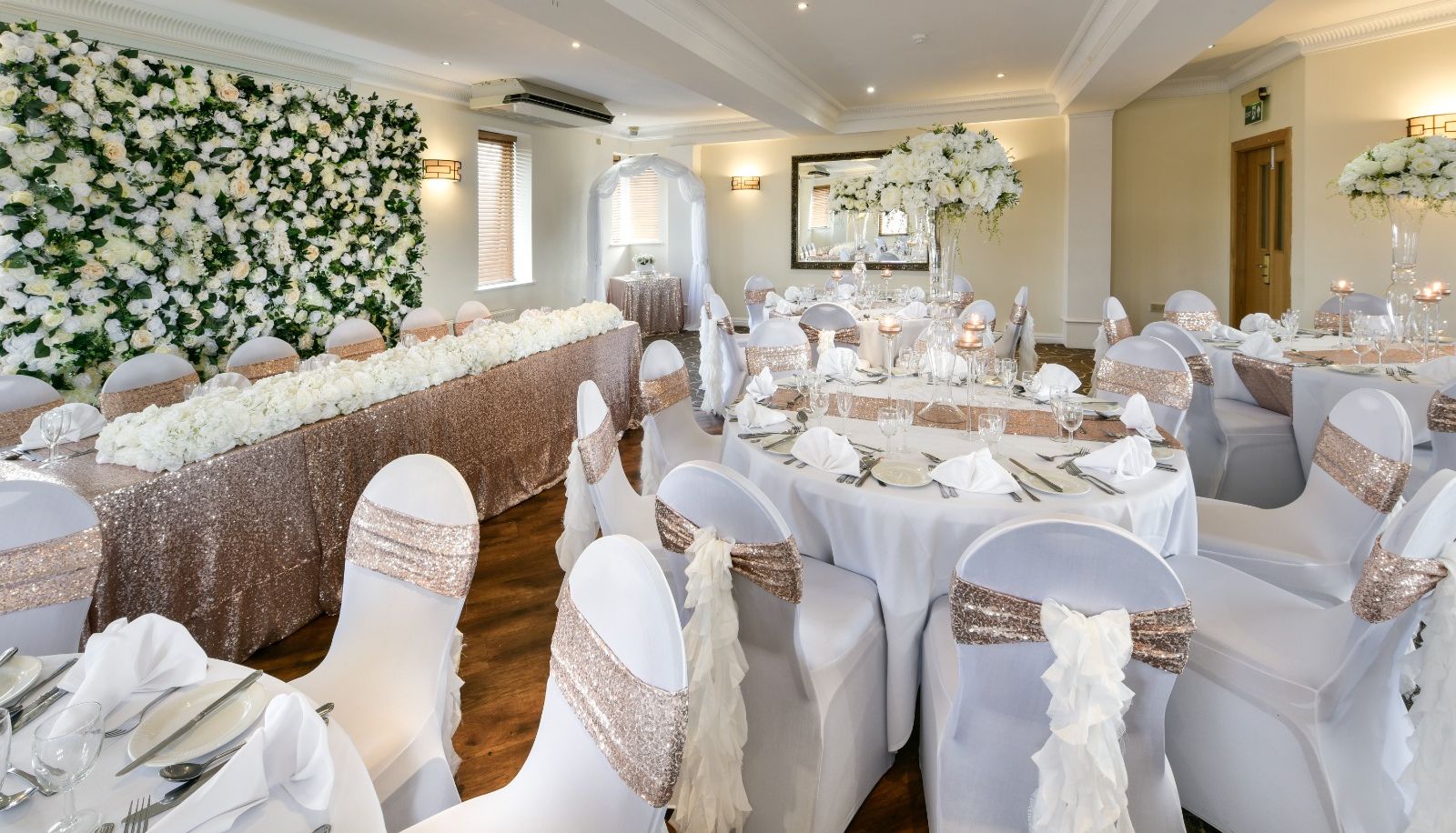 Elegant wedding reception hall with white and gold decor, floral arrangements, and banquet tables.