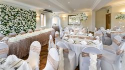 Elegant wedding reception hall with white and gold decor, floral arrangements, and banquet tables.