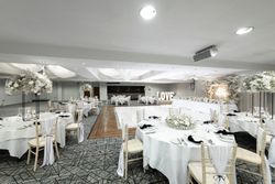 Elegant wedding reception hall decorated in white with round tables, floral centerpieces, draped ceilings, and a large lit-up 'LOVE' sign near a long head table.