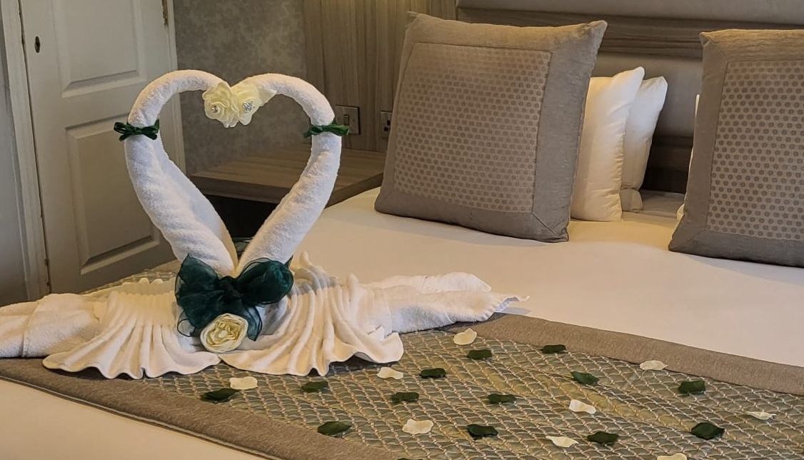 Bed decorated with towel swans shaped into a heart and rose petals