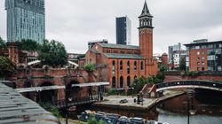 Cityscape featuring a canal, modern skyscraper, and historic brick buildings in Manchester, England