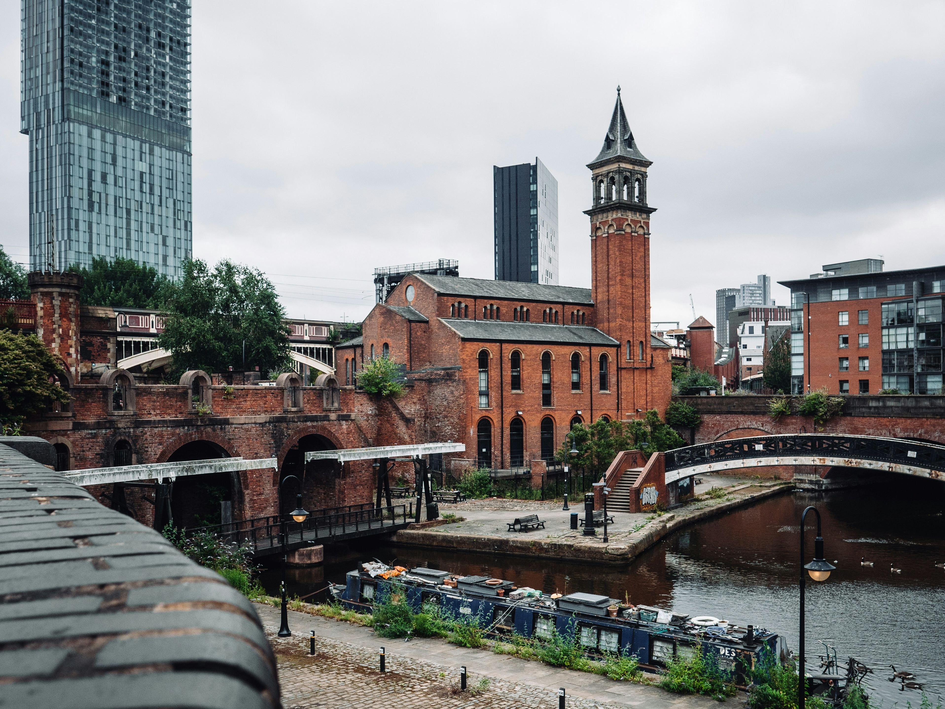 Cityscape featuring a canal, modern skyscraper, and historic brick buildings in Manchester, England