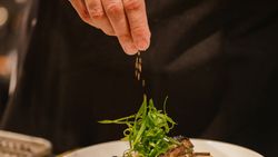 Chef garnishing a plate of grilled meat ribs with green garnish and sesame seeds