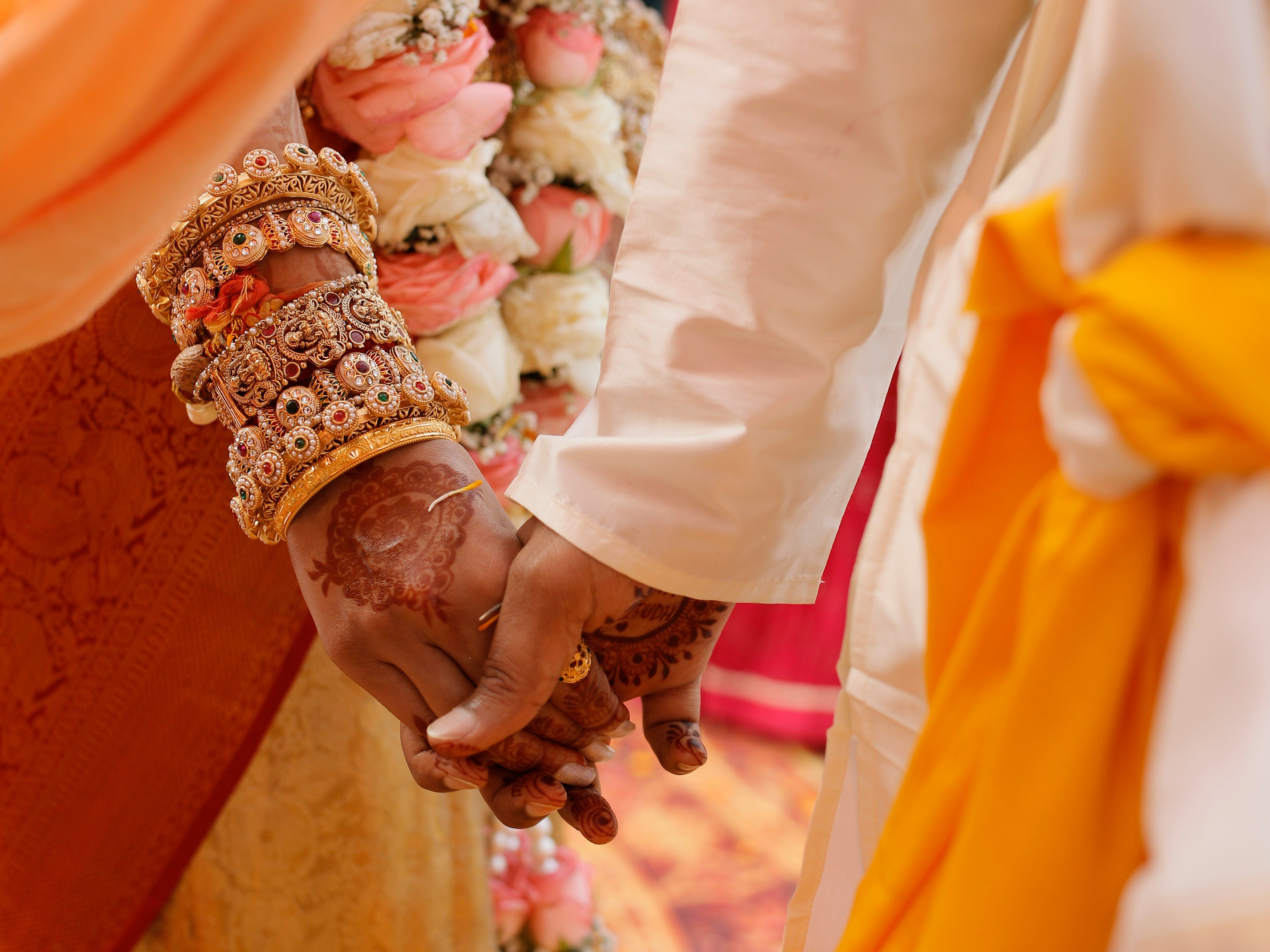 Close-up of a couple holding hands during a traditional Indian wedding ceremony, adorned with intricate jewelry, henna, and colorful garments.