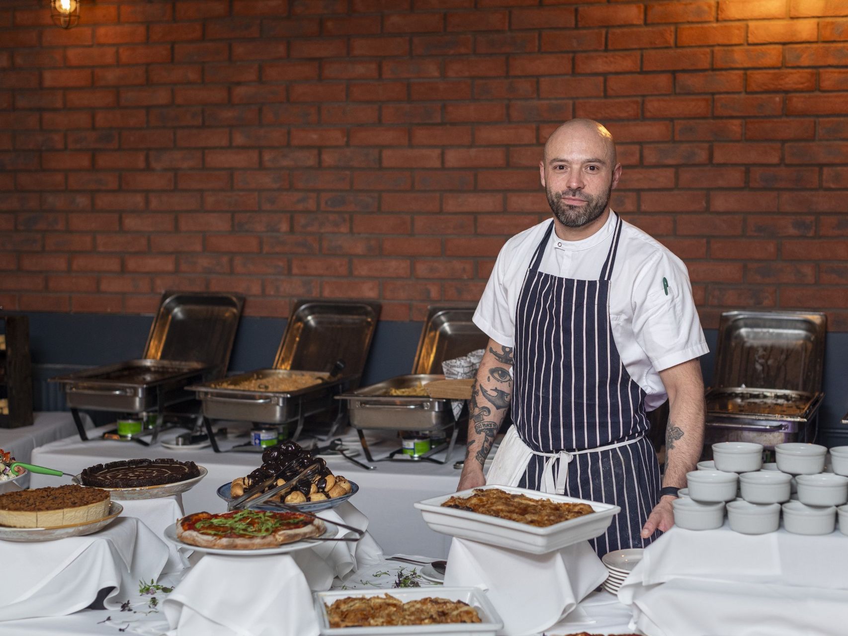 Chef standing behind a buffet table with various dishes and desserts