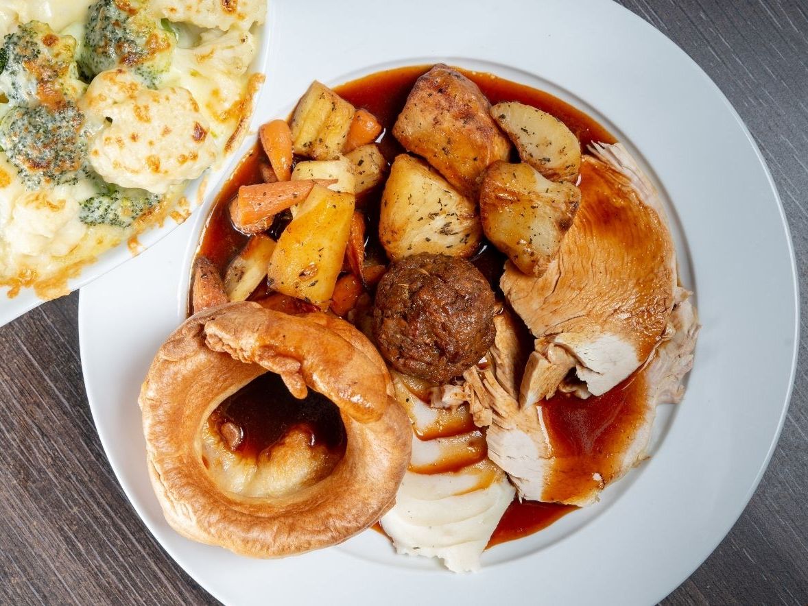 Traditional British roast dinner with turkey, roasted potatoes, mixed vegetables, Yorkshire pudding, stuffing, and gravy, served with a side of cauliflower broccoli cheese.