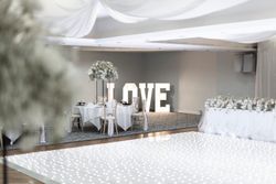Elegant wedding reception hall decorated in white with a sparkling dance floor, large illuminated LOVE letters, round tables set for guests, and floral centerpieces.
