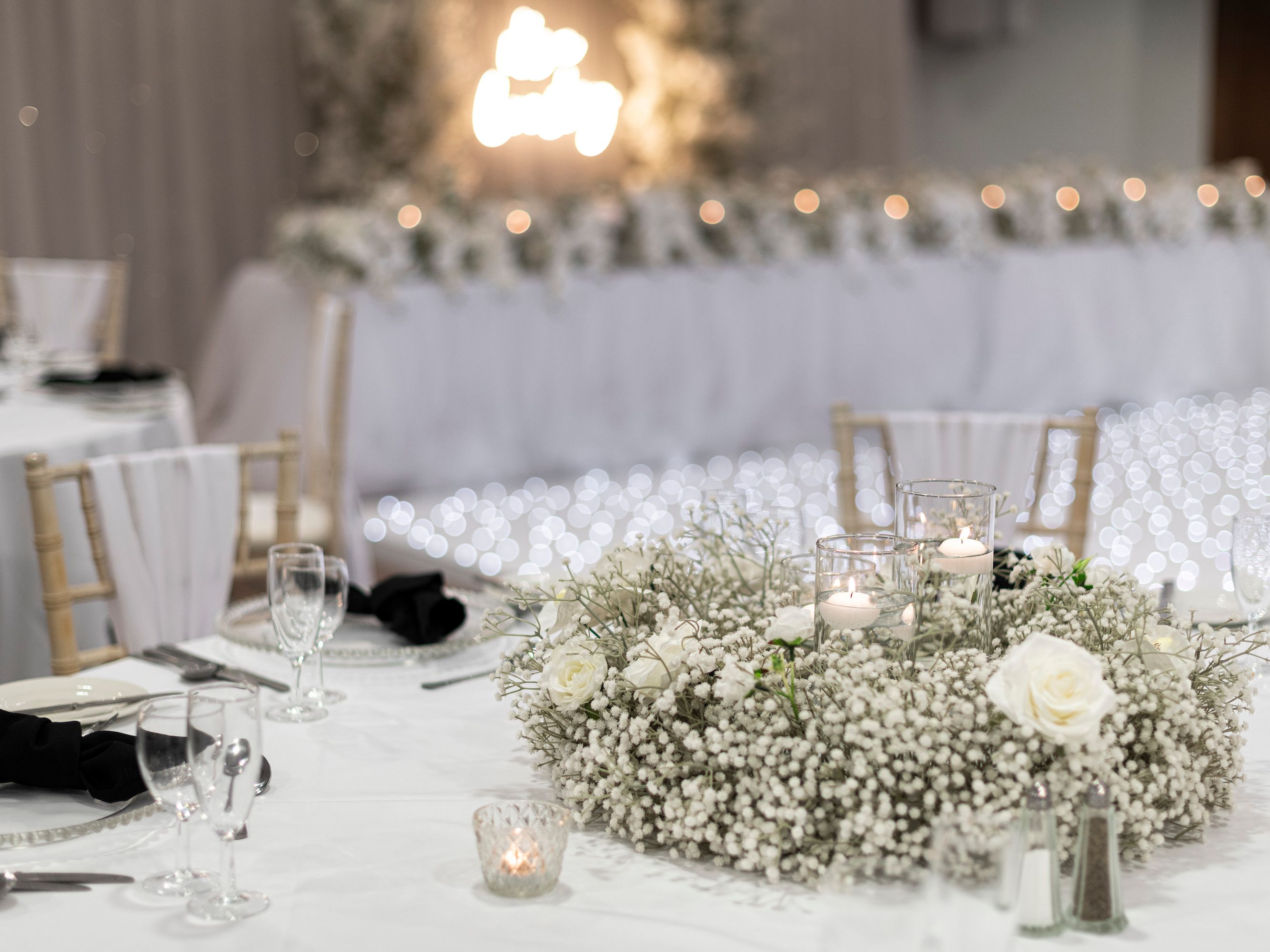 Elegant wedding reception table setting with white flowers, glass candle holders, and soft lighting in a romantic decor.