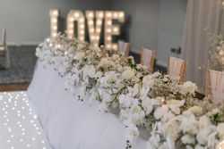 Elegant wedding reception table decorated with white flowers and candles, with illuminated 'LOVE' sign in the background.