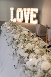 Elegant wedding table decorated with white flowers and candles, with large illuminated LOVE letters in the background.