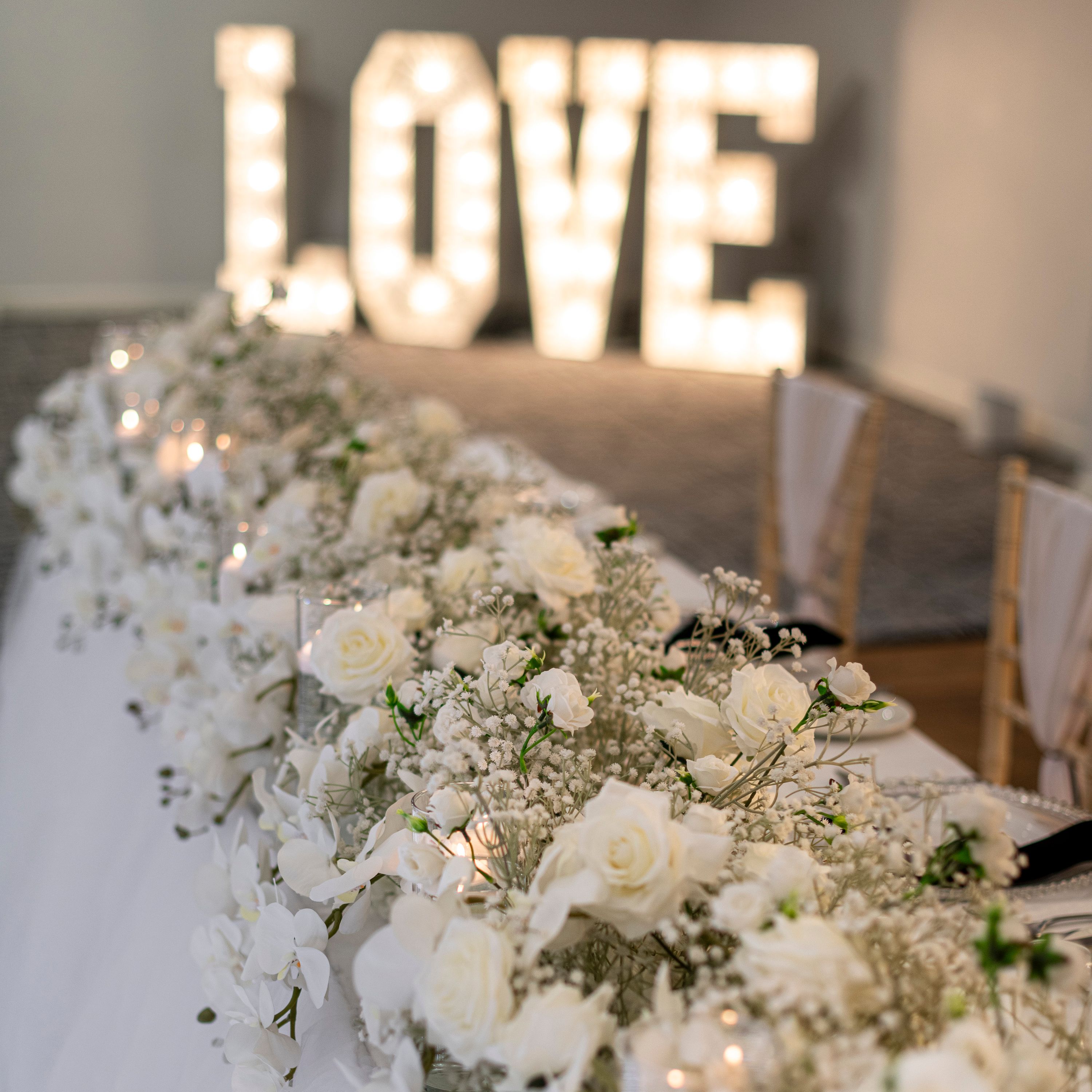 Elegant wedding table decorated with white flowers and candles, with large illuminated LOVE letters in the background.