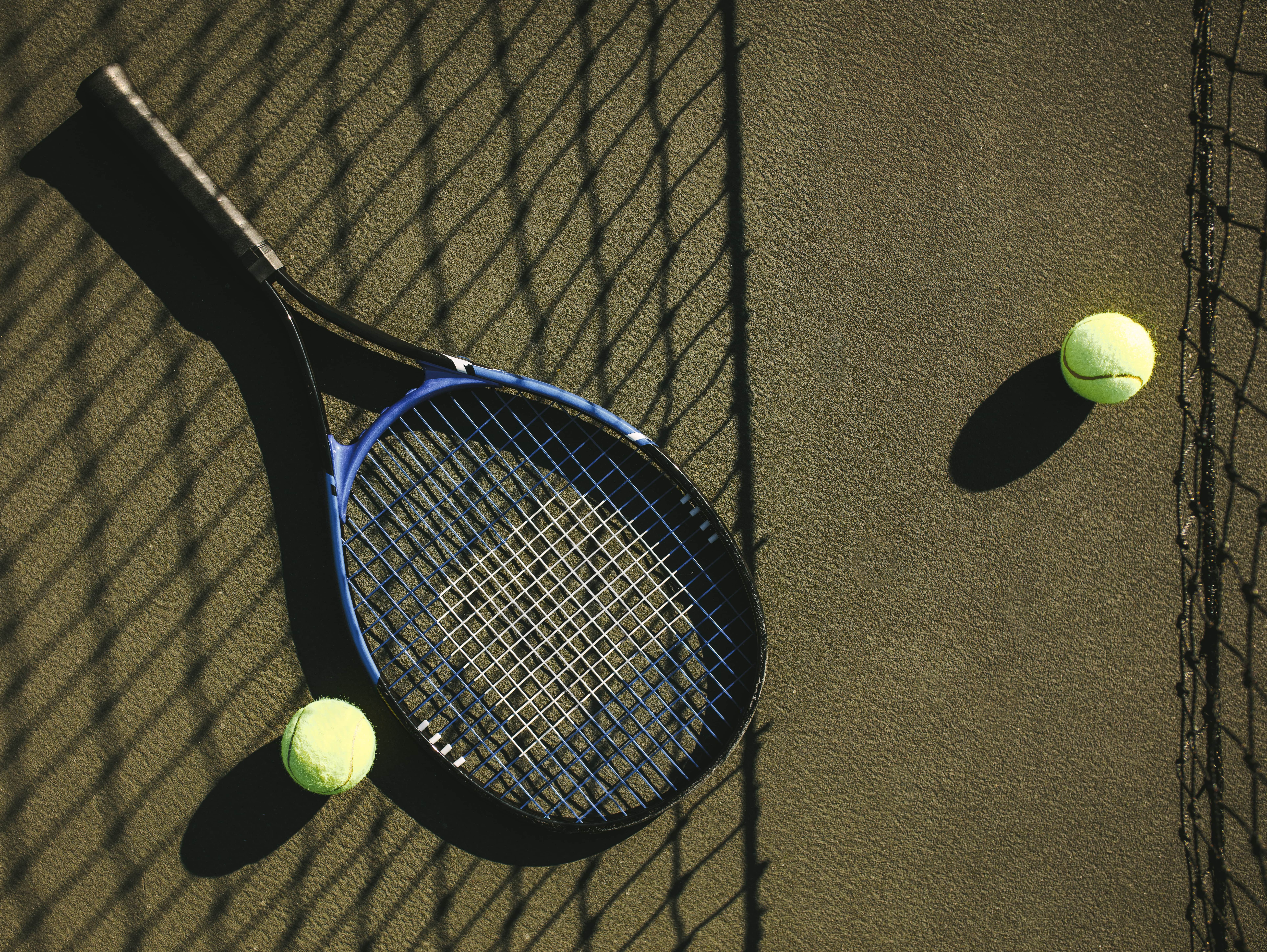 Tennis racket and tennis balls on a court with shadow of net