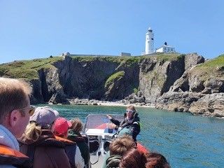 Group of people on a boat tour near a rocky coastline with a white lighthouse on a hill