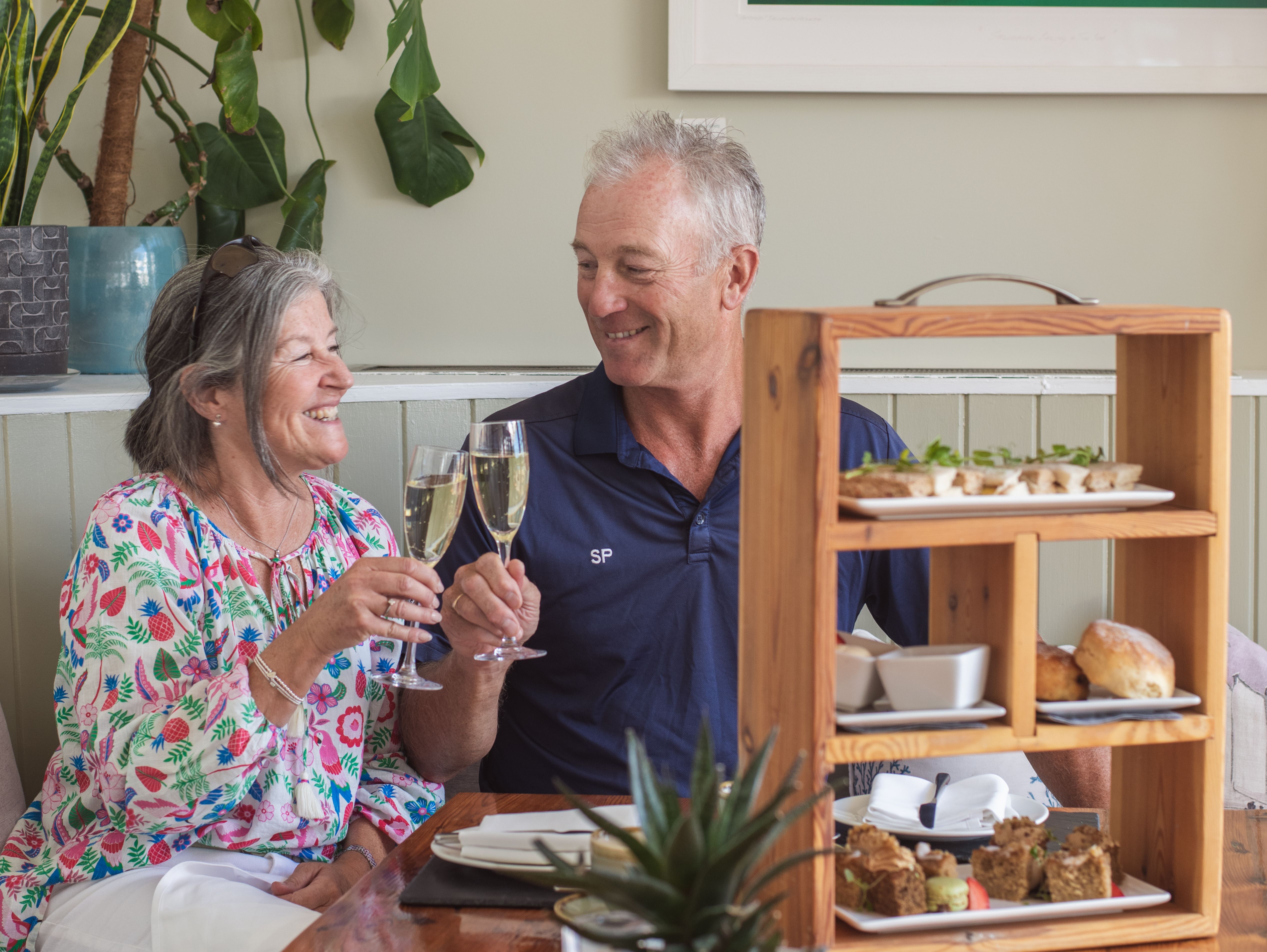 Smiling couple enjoying champagne and afternoon tea treats at a cozy restaurant table