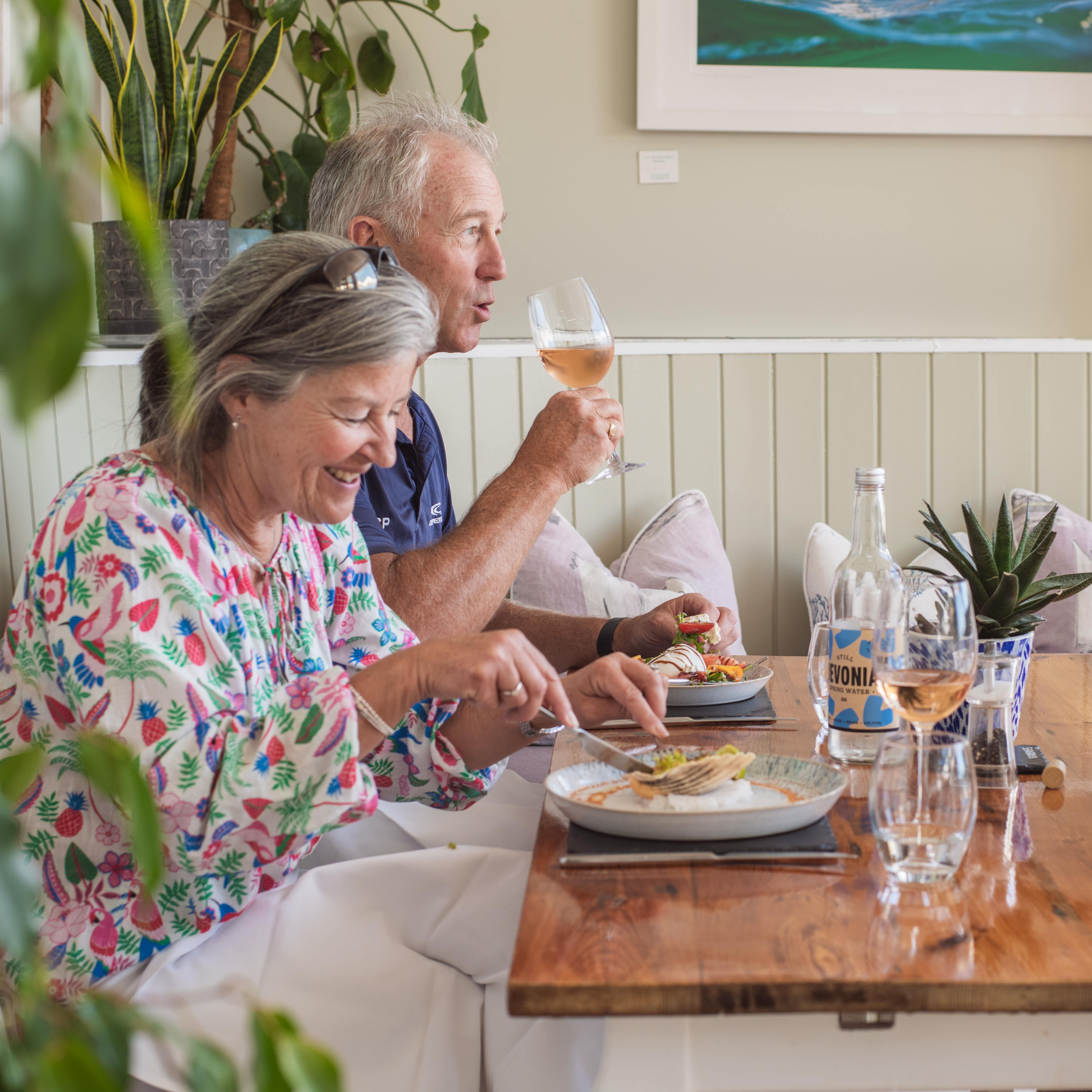 Smiling couple enjoying a meal with wine at a cozy restaurant table.