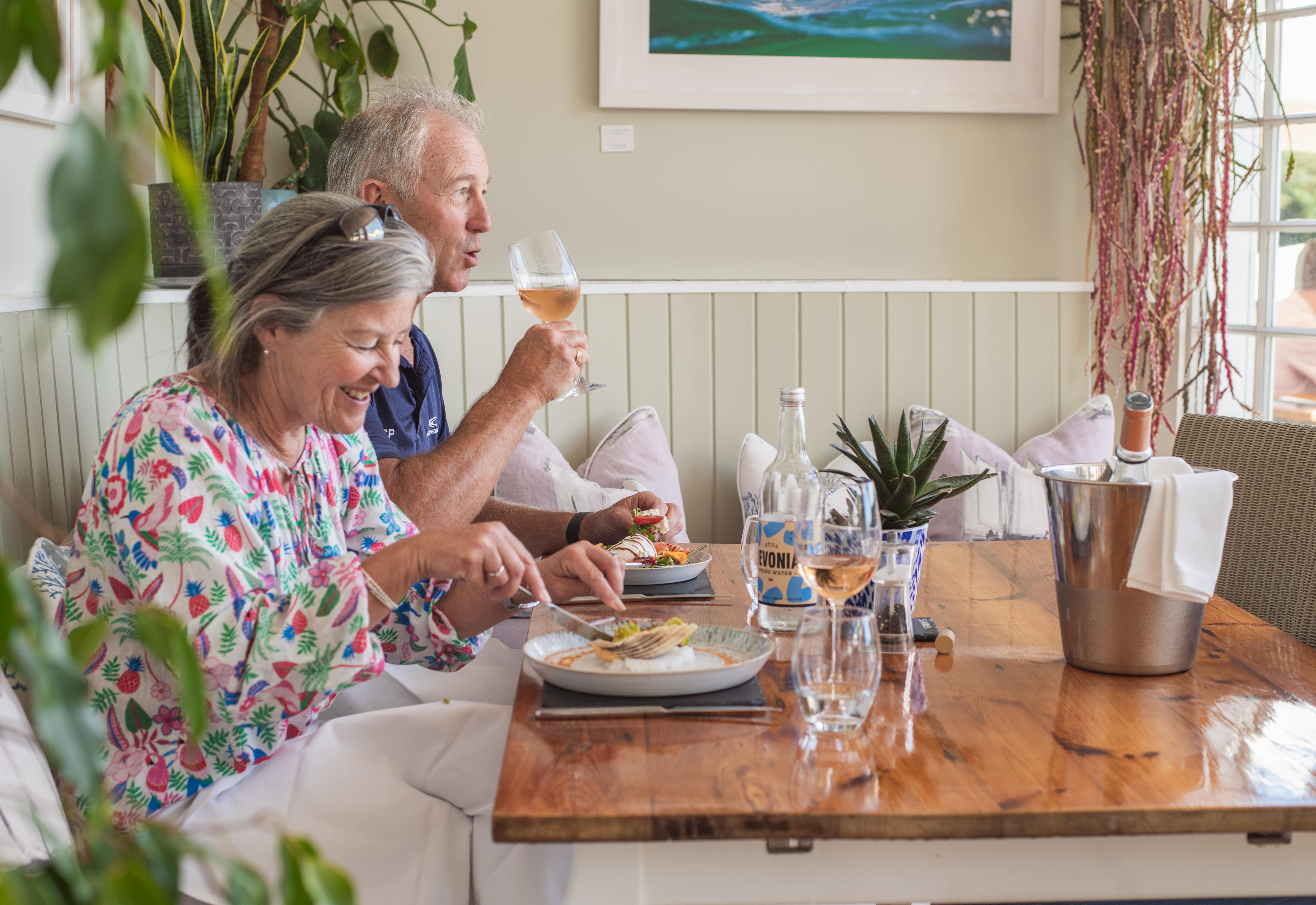 Smiling couple enjoying a meal with wine at a cozy restaurant table.
