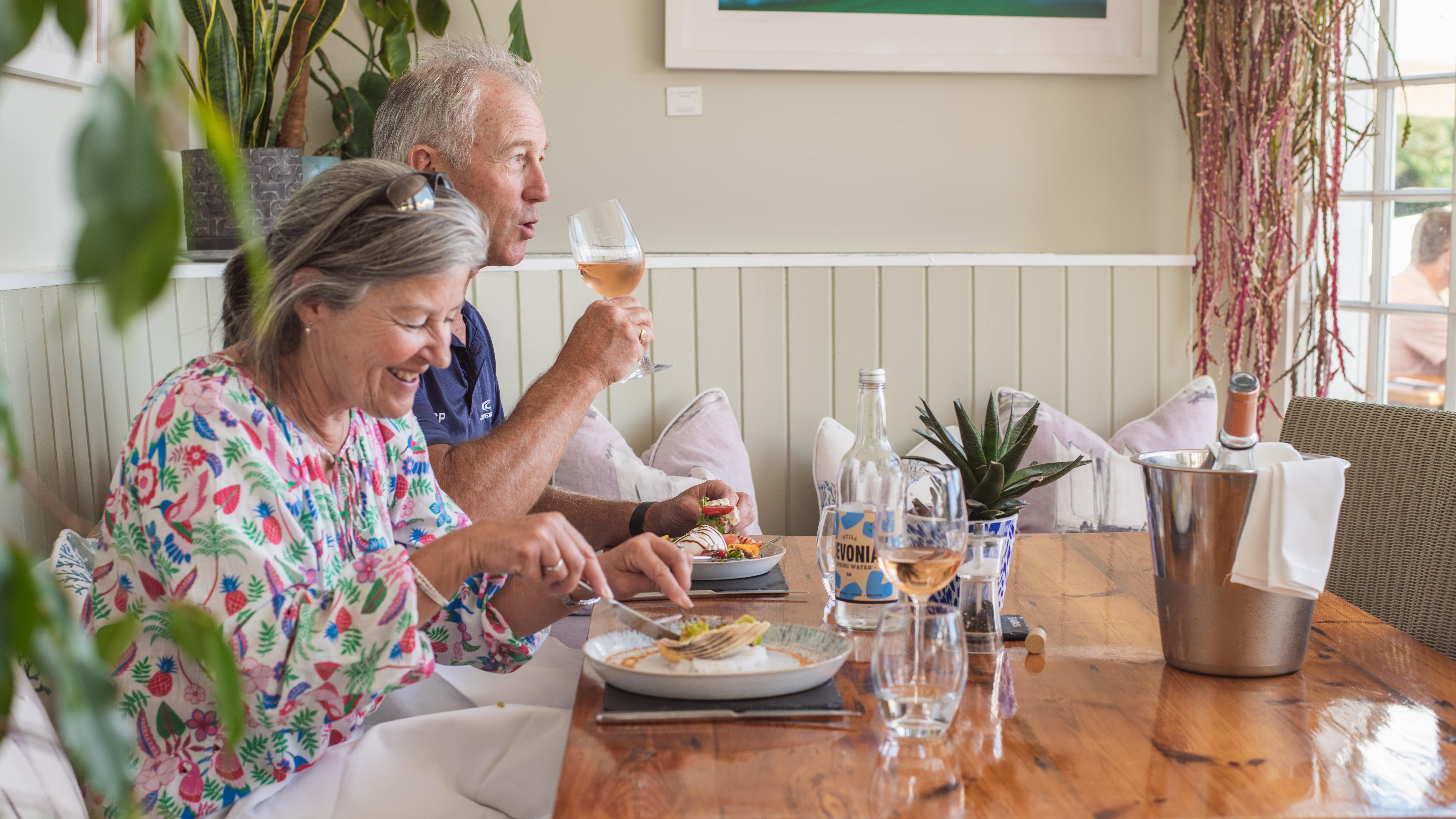 Smiling couple enjoying a meal with wine at a cozy restaurant table.