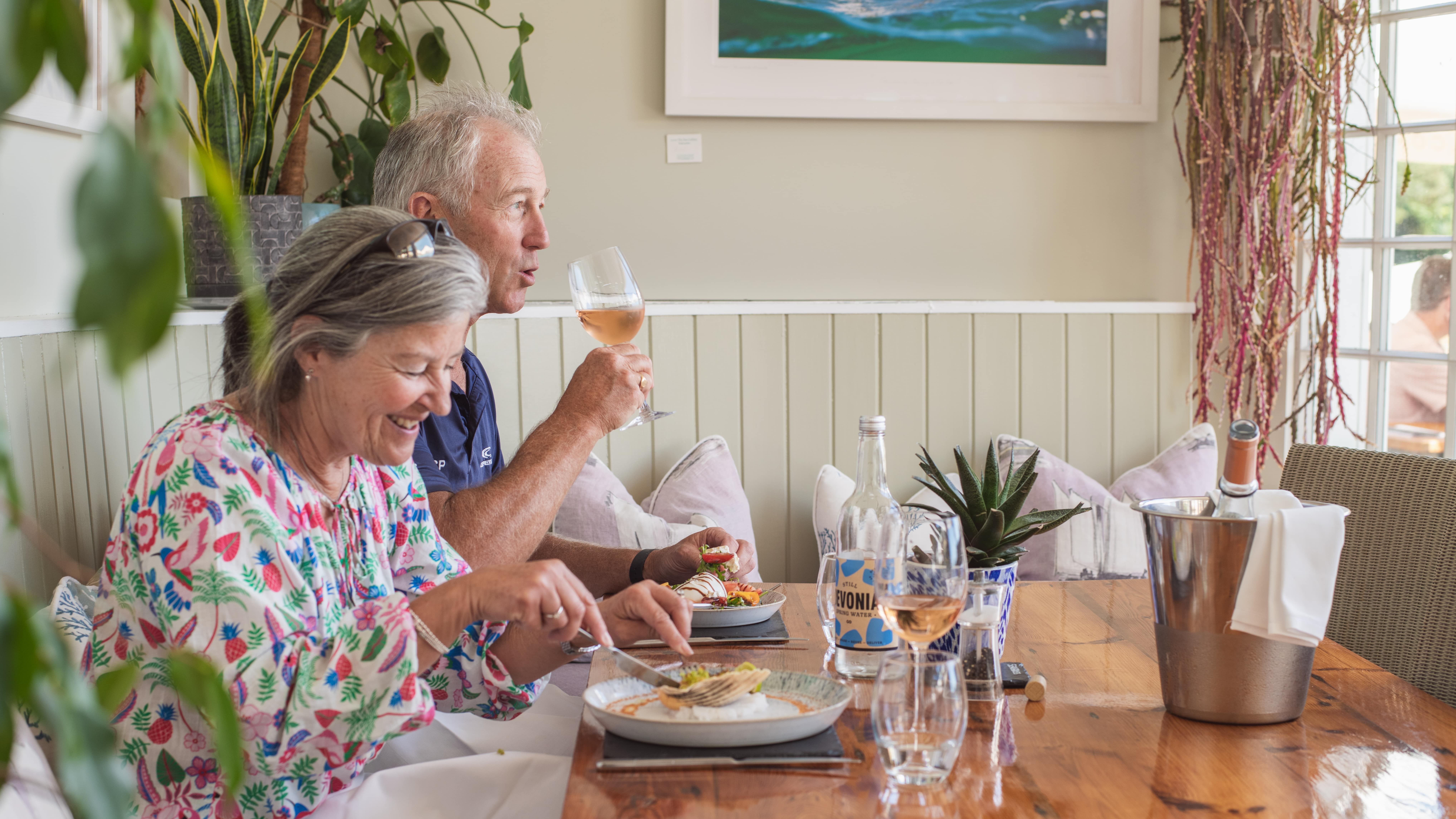 Smiling couple enjoying a meal with wine at a cozy restaurant table.