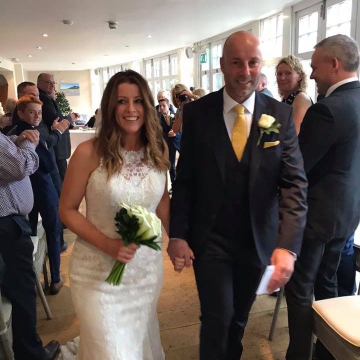 Bride and groom walking down the aisle at an indoor wedding ceremony, holding hands and smiling.