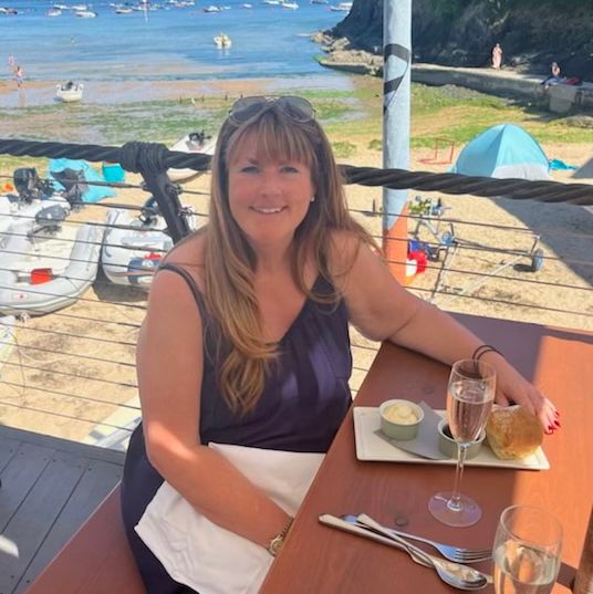 Woman sitting at an outdoor restaurant table by the beach with food and a glass of wine.