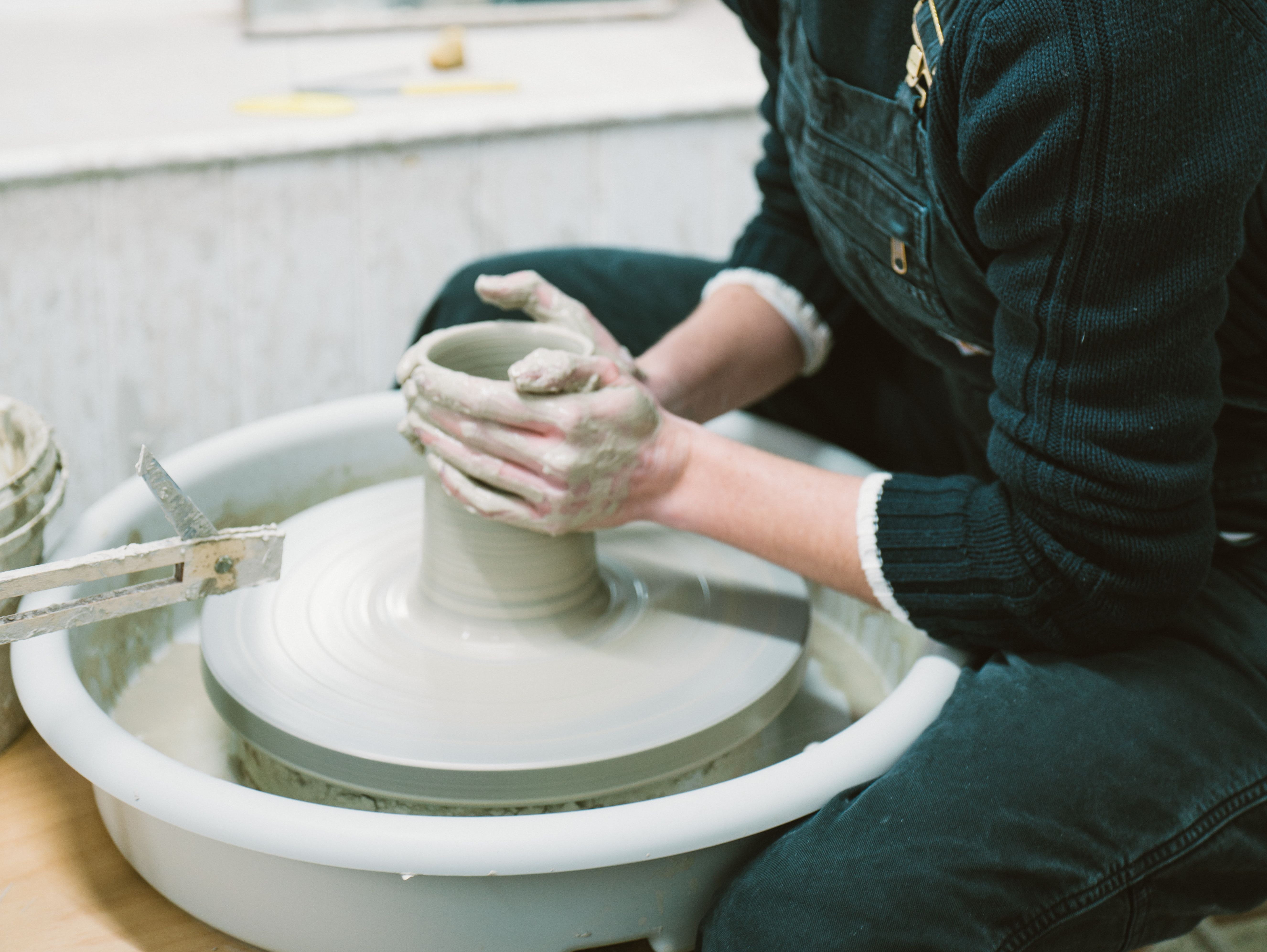 Woman shaping a clay pot on a pottery wheel in a studio
