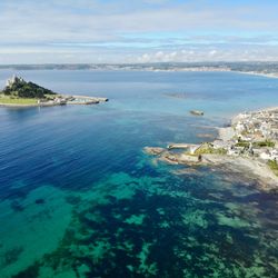 Aerial view of St Michael's Mount, a tidal island with a castle, connected by causeway to a coastal village in Cornwall, UK.