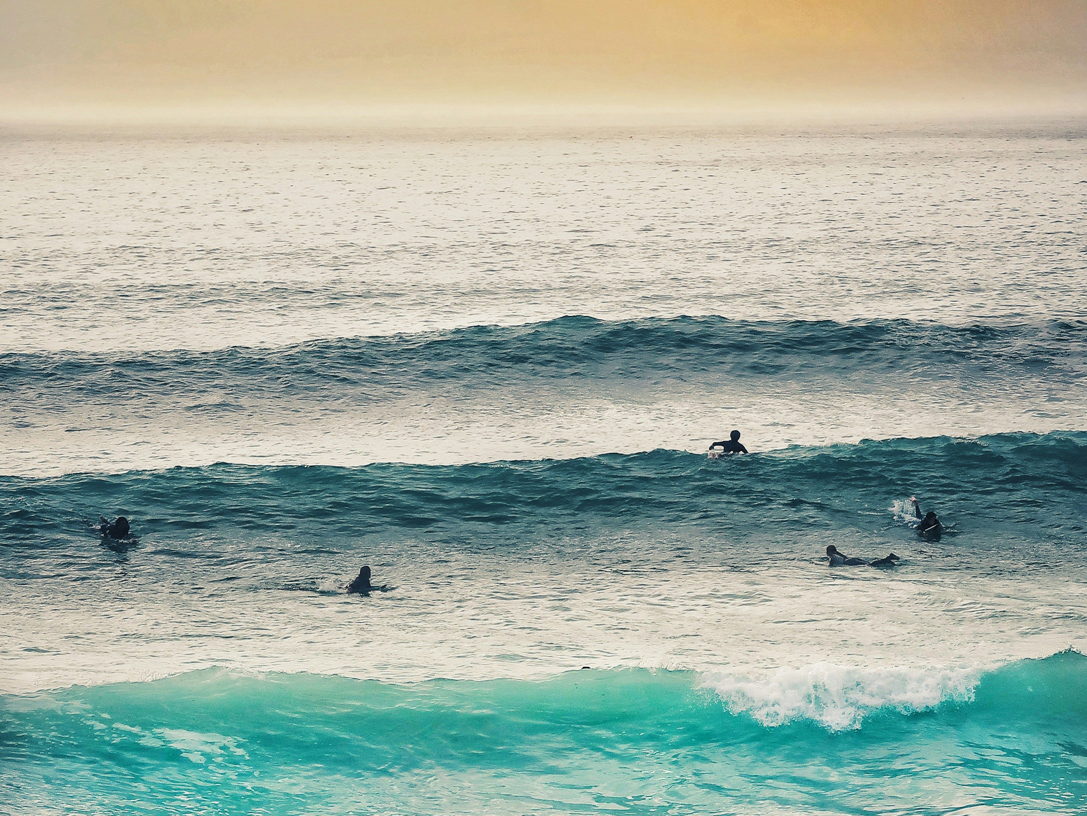 Surfers in the ocean waiting for waves under a cloudy orange sunset sky.