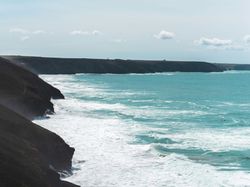 Rocky coastline with waves crashing against cliffs under a partly cloudy sky.
