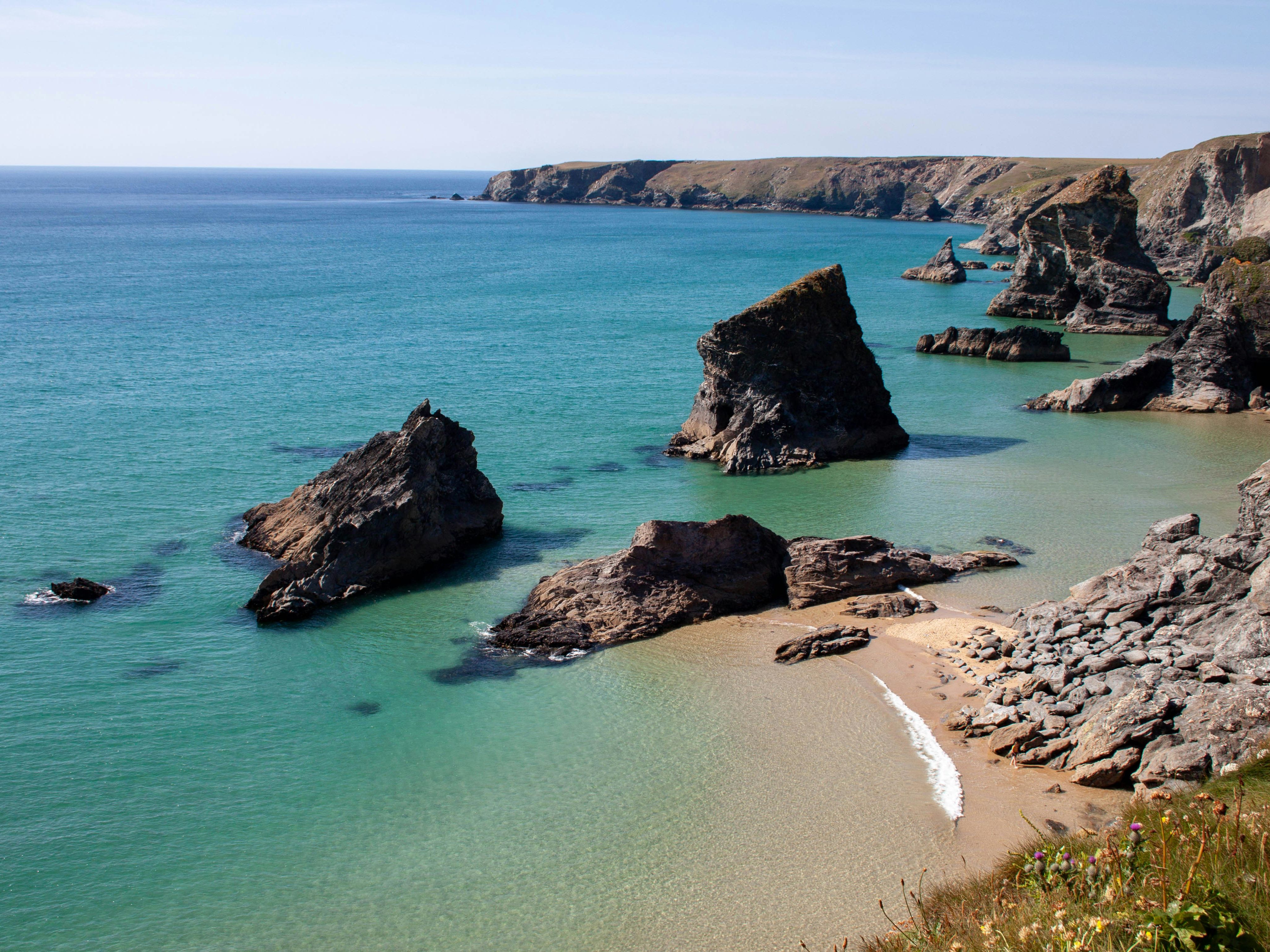 Rock formations and cliffs along a turquoise coastal bay with clear blue water and a sandy beach.