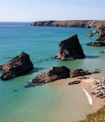 Rock formations and cliffs along a turquoise coastal bay with clear blue water and a sandy beach.