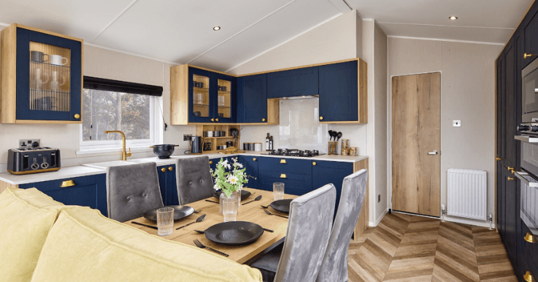 Modern kitchen and dining area with blue cabinets, wooden accents, a set dining table with black plates, and herringbone wood flooring.