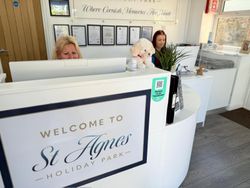 Reception area at St Agnes Holiday Park with two people at the front desk, certificates on the wall, and a stuffed dog toy on the counter.