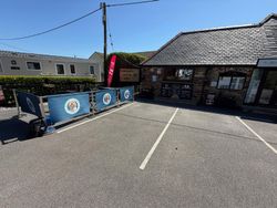 Outdoor seating area in front of a small coffee shop called Charlie's Coffee Pod, with a signboard and menu on display, located next to a stone building on a sunny day.