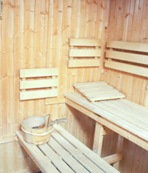 Interior of a traditional wooden sauna with benches, a water bucket, and sauna stones.
