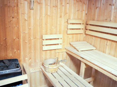Interior of a traditional wooden sauna with benches, a water bucket, and sauna stones.