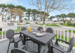 Outdoor dining setup on a deck with a view of holiday park cabins
