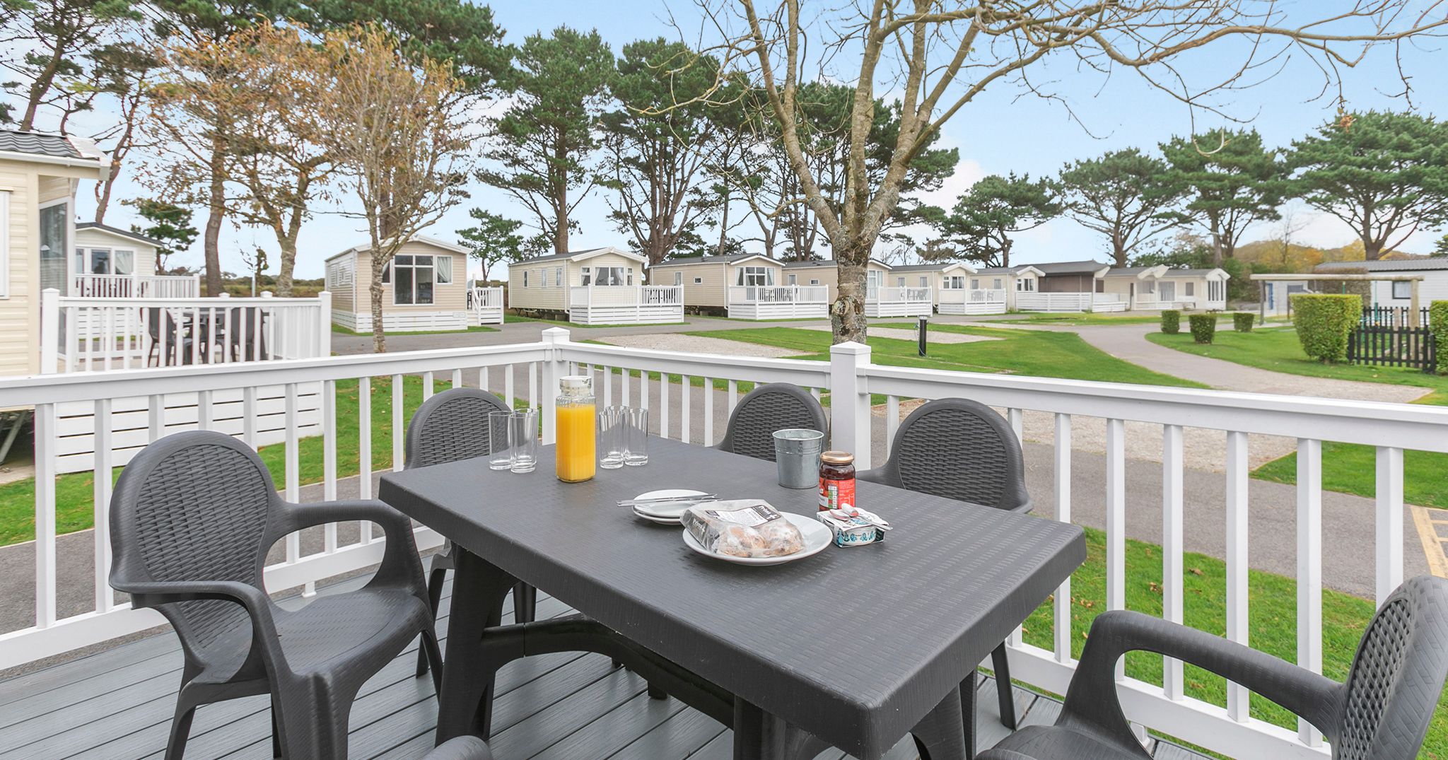 Outdoor dining setup on a deck with a view of holiday park cabins