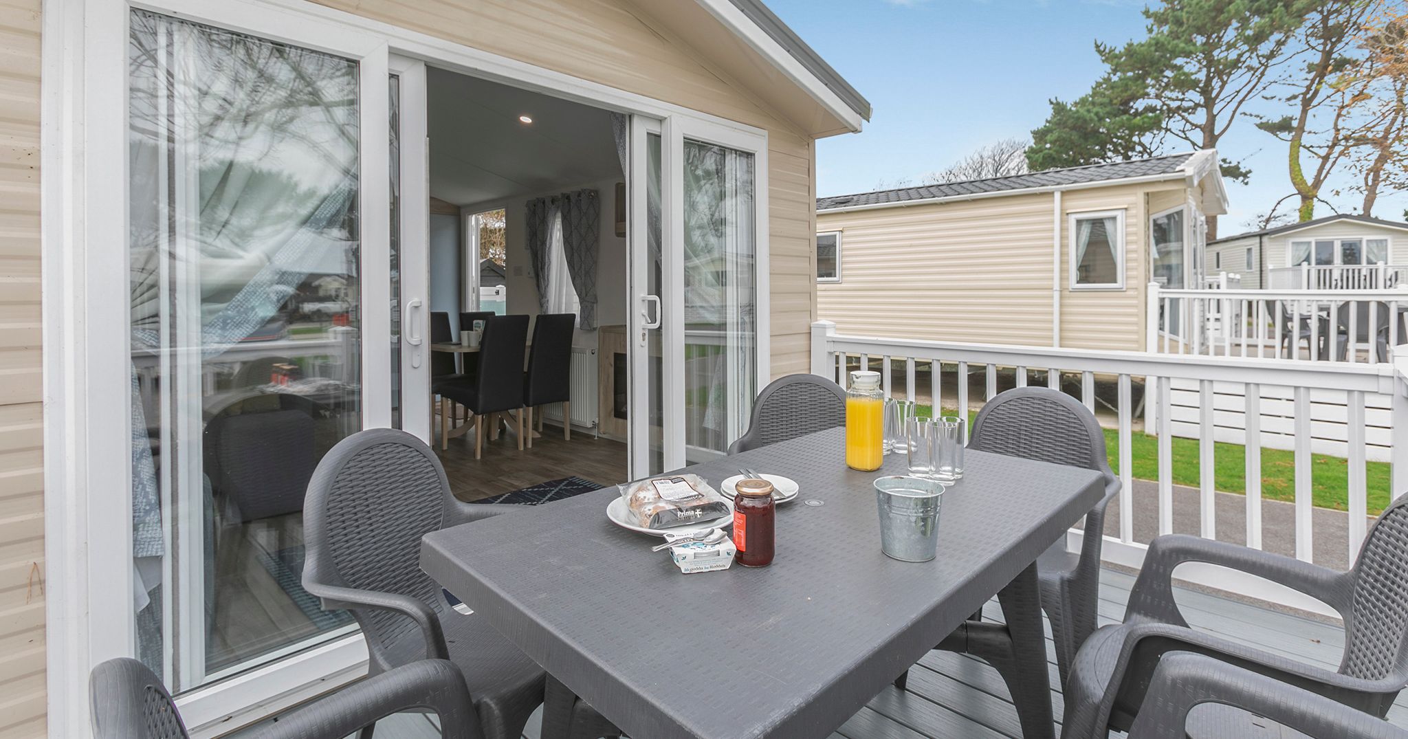 Outdoor patio area of a mobile home with a table, chairs, breakfast items, and sliding doors leading inside
