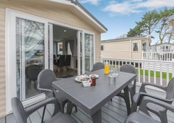 Outdoor patio area of a mobile home with a table, chairs, breakfast items, and sliding doors leading inside