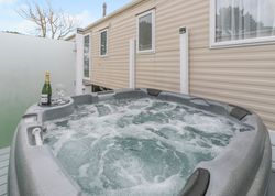 Outdoor hot tub next to a beige mobile home with champagne and glasses on the edge.