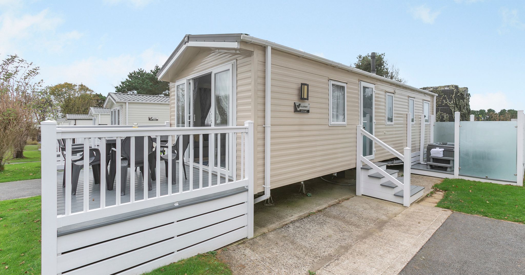 Modern beige mobile home with white railings and patio chairs