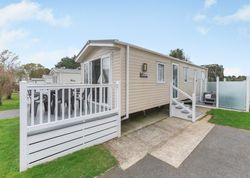 Modern beige mobile home with white railings and patio chairs