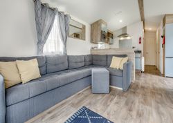 Modern living area with an L-shaped grey sofa, light wood floors, and open kitchen.