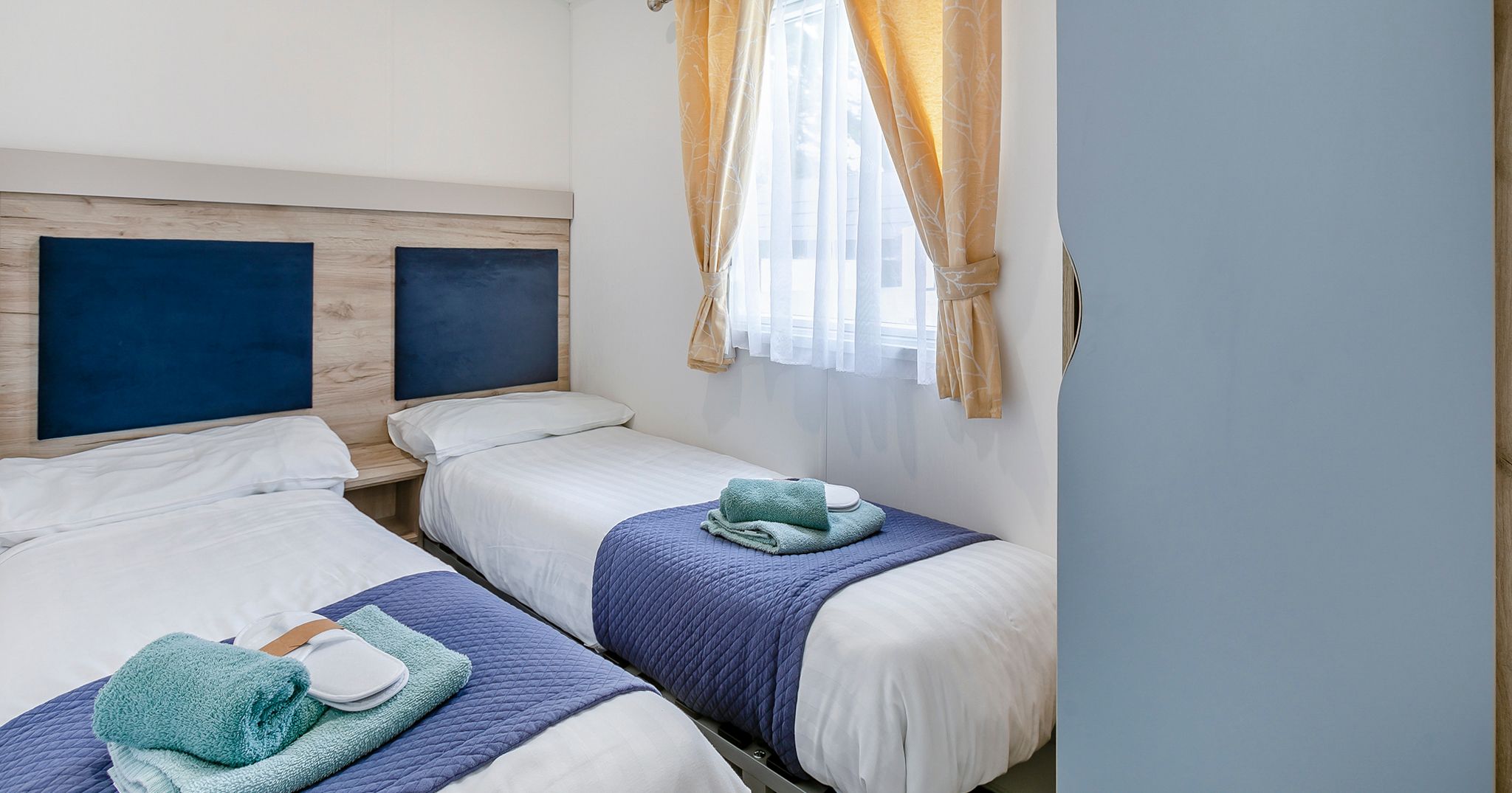 Twin bedroom with two single beds, blue accents, and a window with yellow curtains