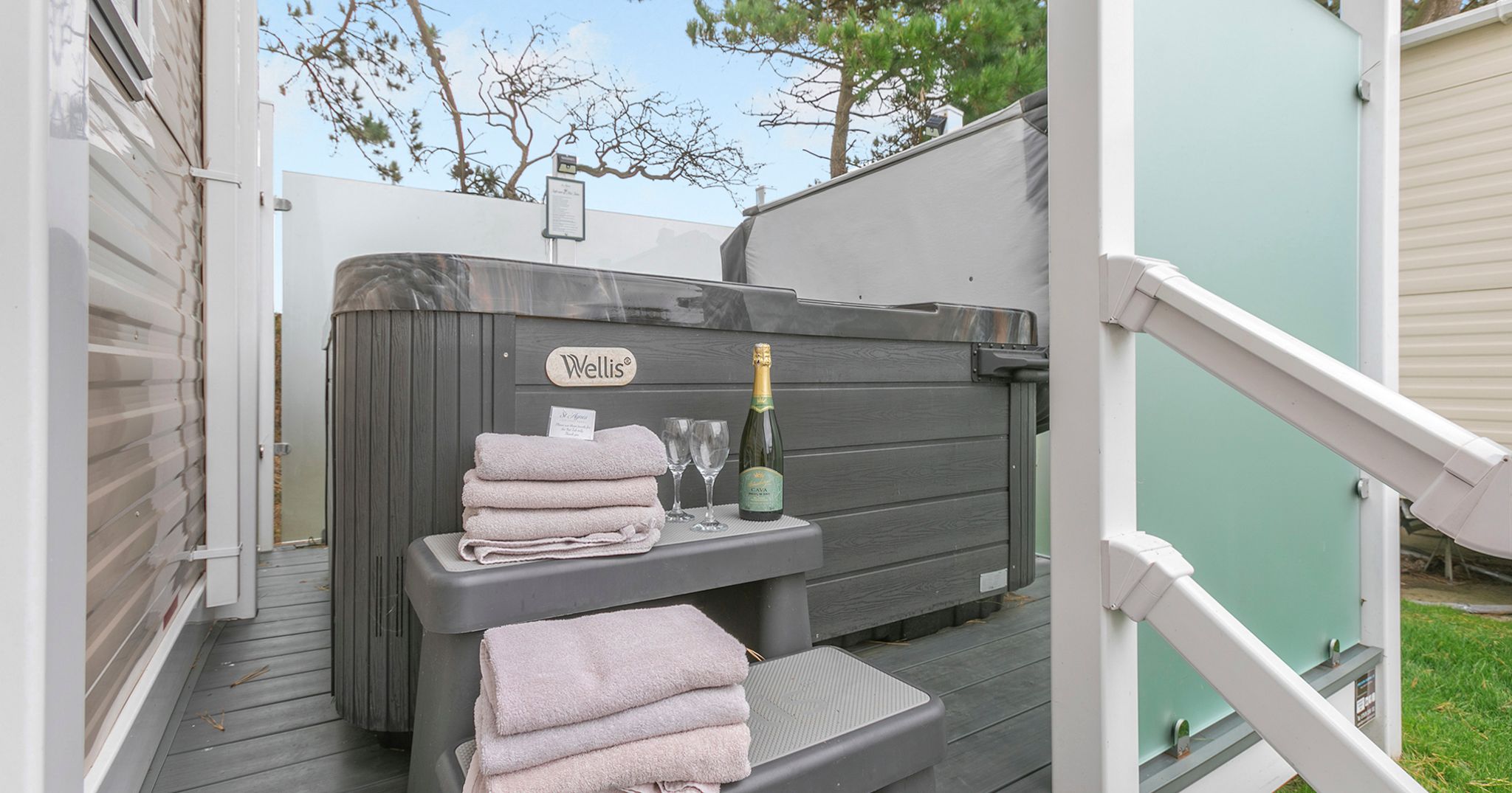 Outdoor hot tub with folded towels, champagne, and glasses on steps.