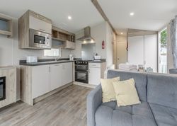 Modern kitchen and living area inside a mobile home with grey sofa and light wood flooring