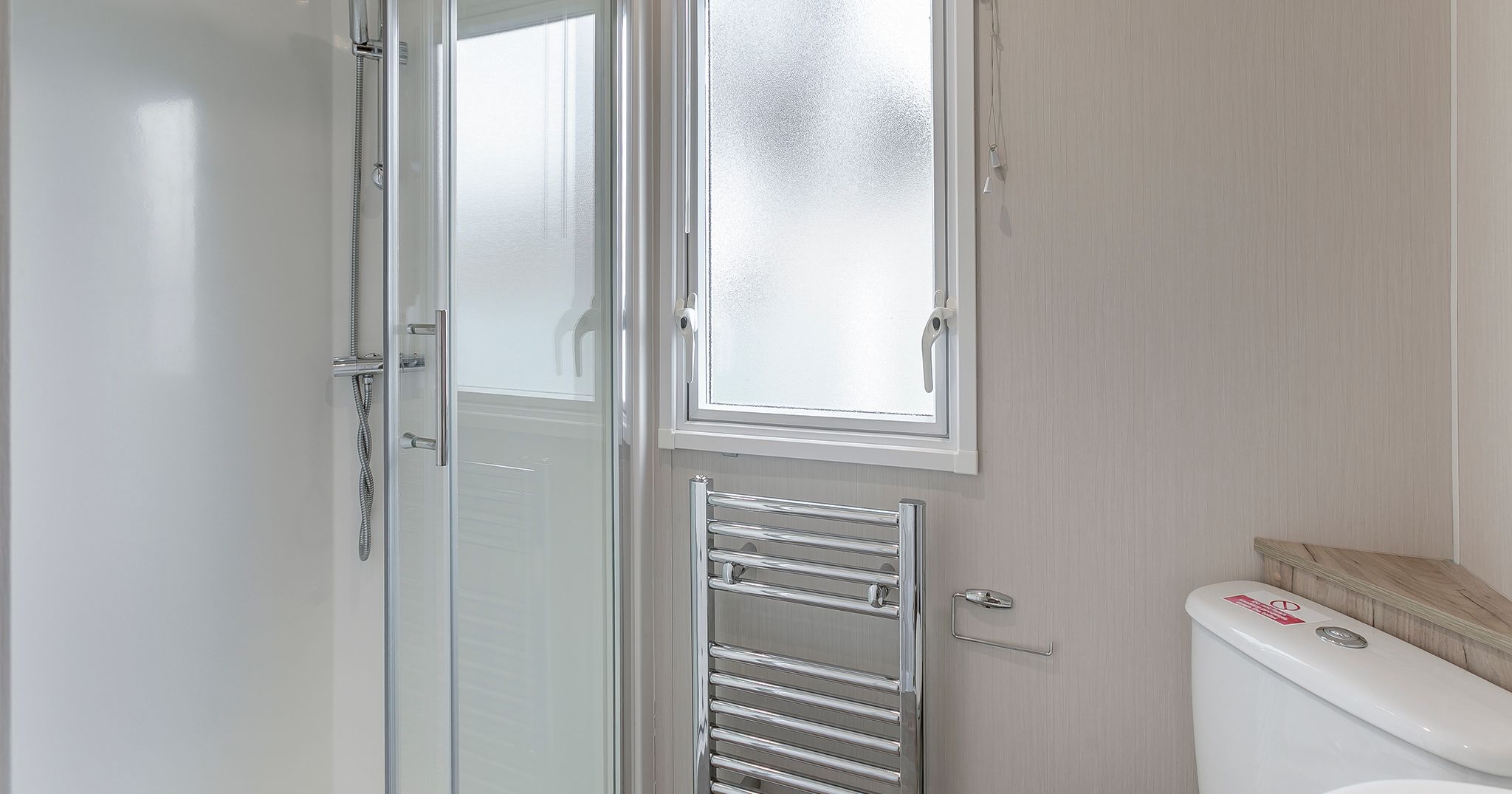 Modern bathroom with glass shower, frosted window, towel radiator, and toilet