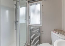 Modern bathroom with glass shower, frosted window, towel radiator, and toilet