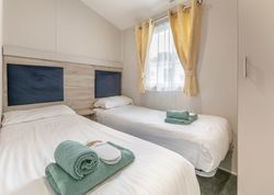 Modern twin bedroom with two single beds, white linens, and yellow curtains.