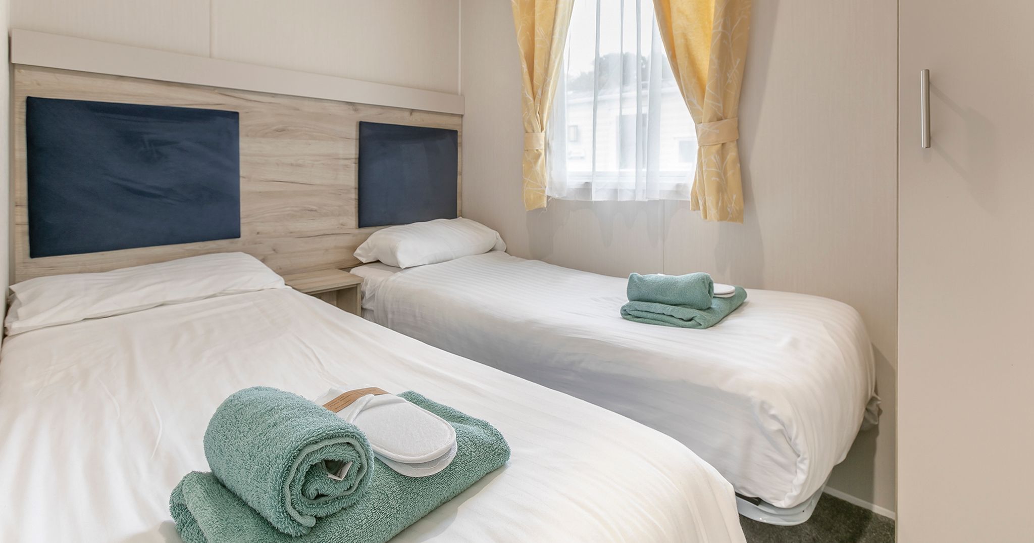 Modern twin bedroom with two single beds, white linens, and yellow curtains.